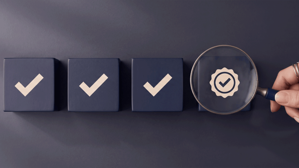 Hand holding magnifying glass over check mark cubes. Quality assurance and business compliance concept.